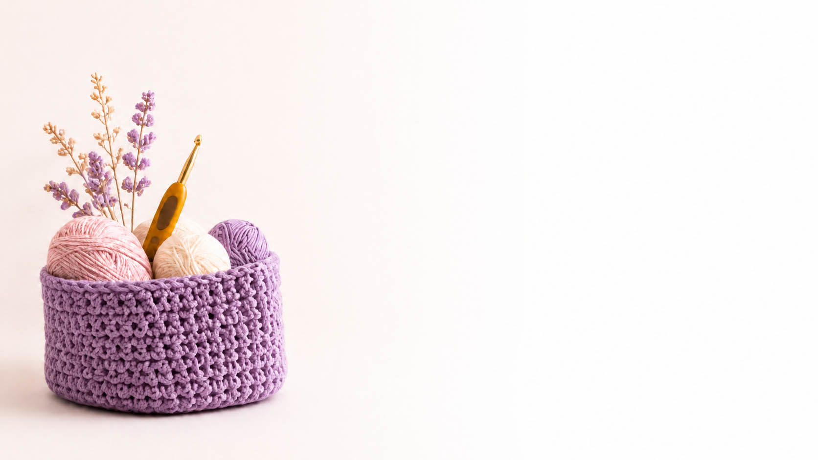 Cesta tejida a crochet con unos ovillo, un ganchillo y una rama de lavanda dentro